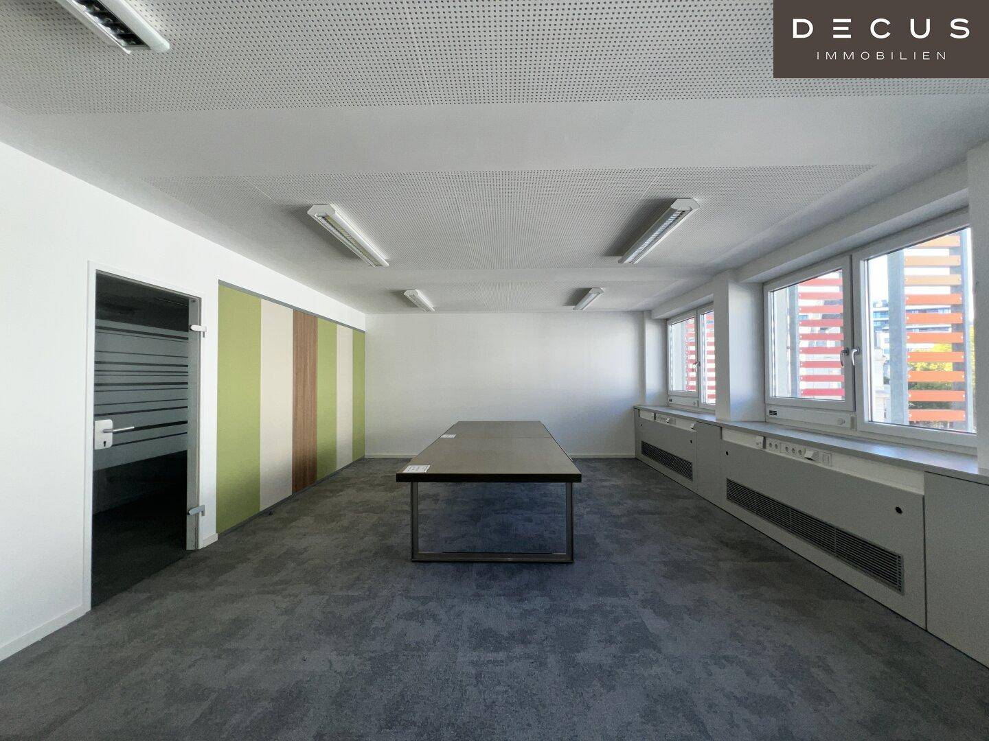 Großes, modernes Büro oder Konferenzraum mit Teppichboden und einem langen Tisch in der Mitte.