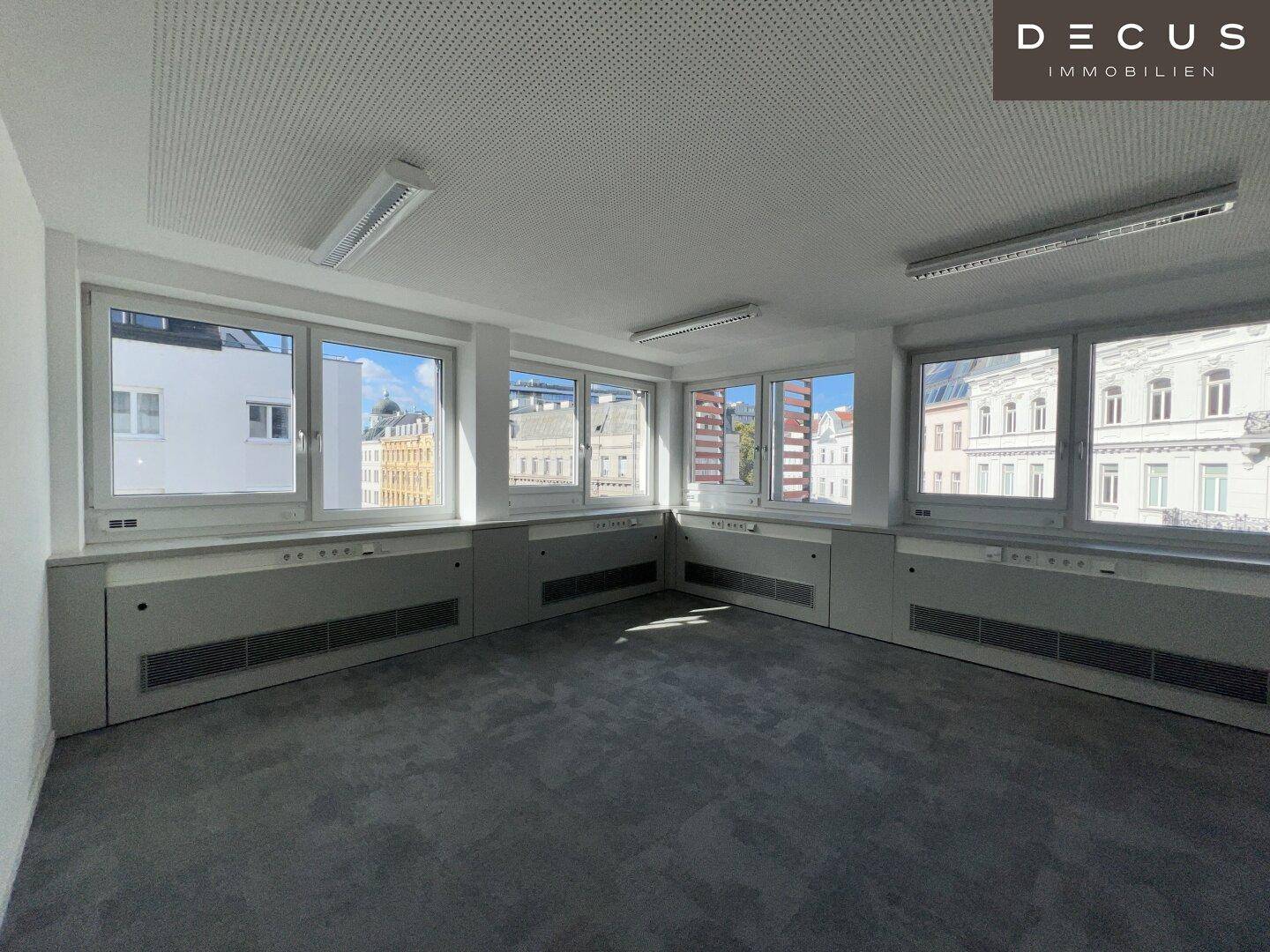 Helles und sauberes Büro mit grauen Teppichfliesen und einer Reihe von Fenstern mit Stadtblick.