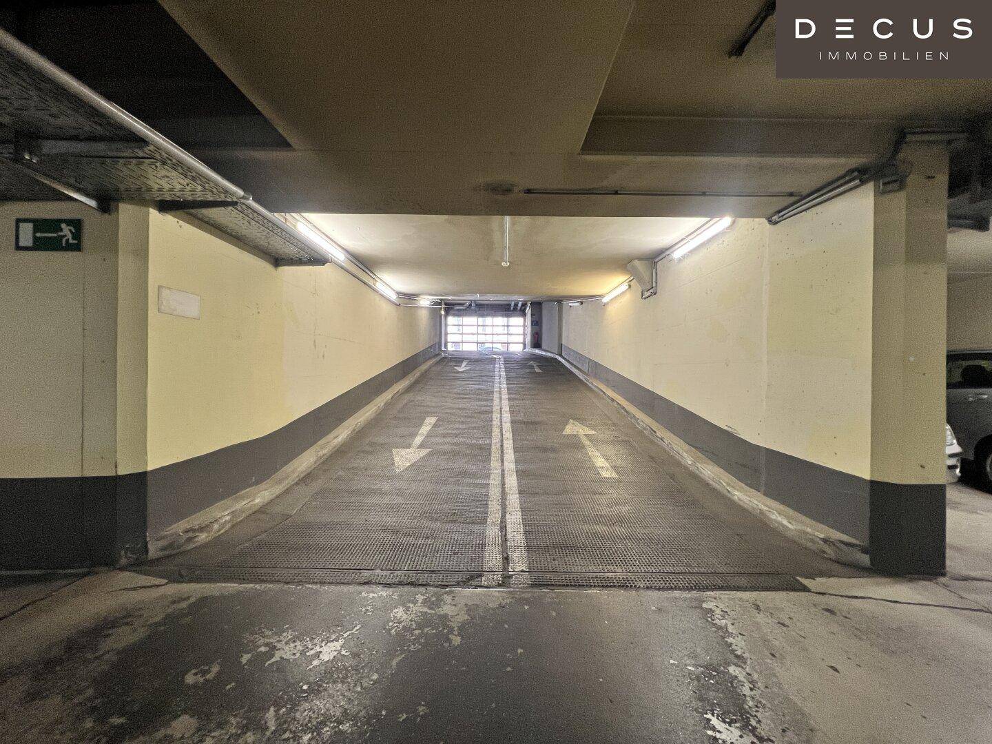 Steile Rampe führt in die Tiefgarage mit klaren Fahrbahnmarkierungen und Beleuchtung.