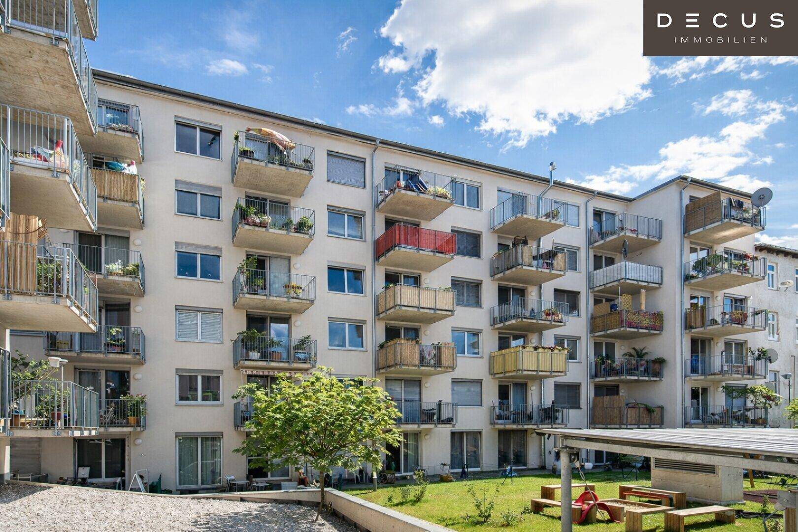 Außenansicht eines Wohnkomplexes mit vielen Balkonen und einem gepflegten Gemeinschaftsgarten mit Spielbereich.