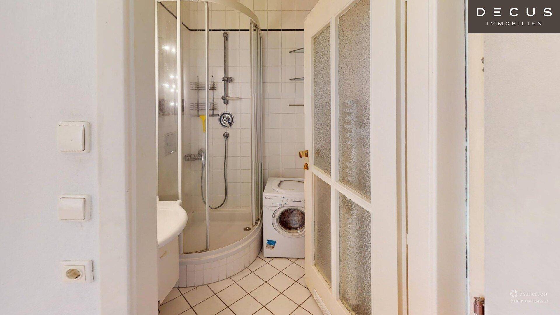 Funktionales Badezimmer mit Duschkabine und Platz für eine Waschmaschine, hell gefliest.