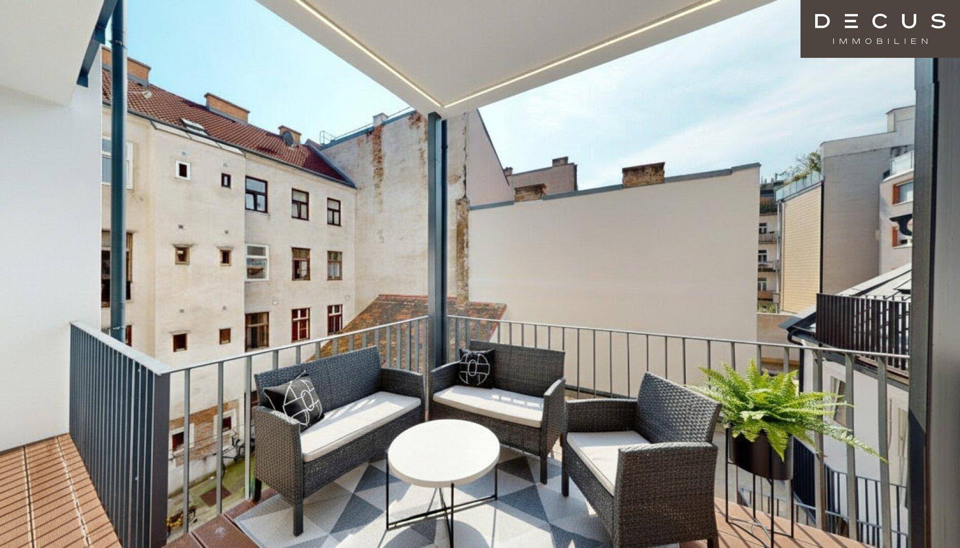 Möblierter Balkon mit Rattanmöbeln und gemustertem Teppich, umgeben von Stadtgebäuden.