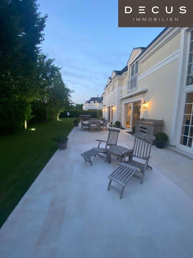 Weitläufige Terrasse mit bequemen Gartenliegen und gepflegtem Rasen im Abendlicht.