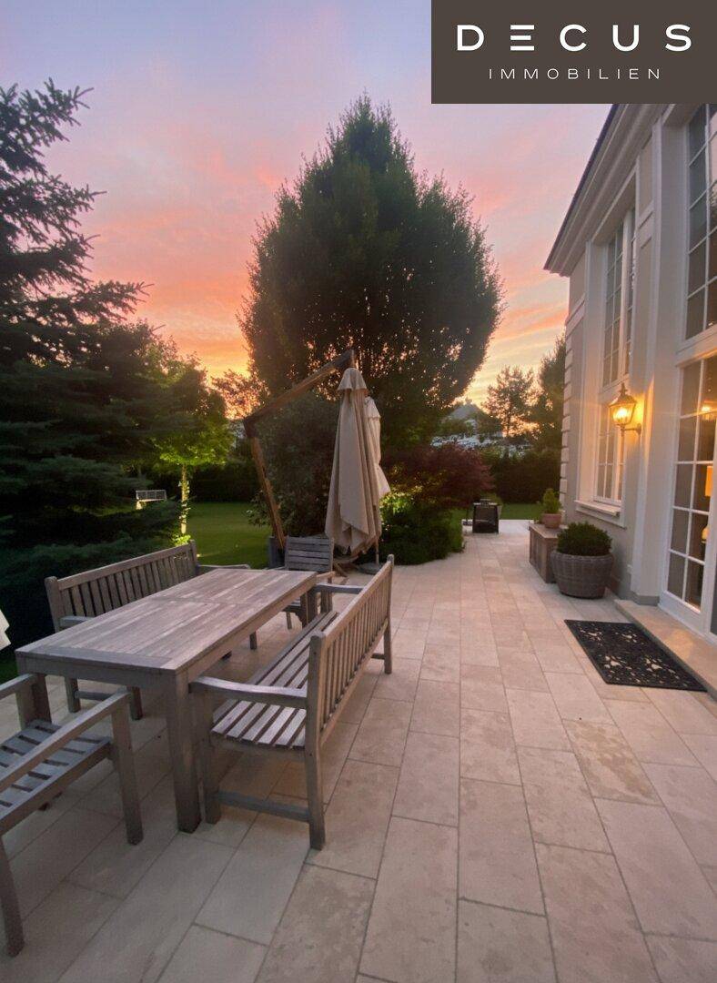 Idyllische Terrasse mit Holzesstisch und Bäumen im Hintergrund, beleuchtet vom Sonnenuntergang.