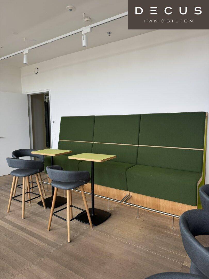 Gemütlicher Loungebereich mit grüner Sitzbank, kleinen Tischen und Holzboden.
