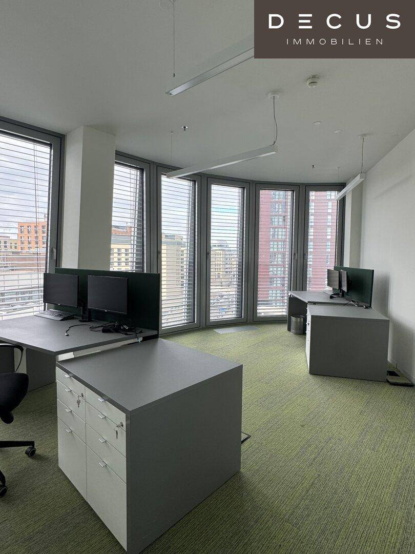 Büroarbeitsplätze in einem hellen Raum mit gebogenen Fensterfronten und Blick auf die Stadt.
