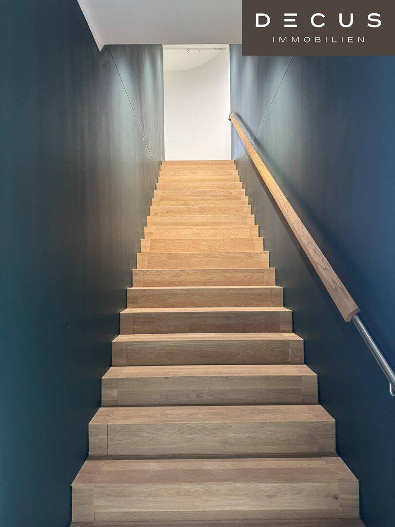 Elegante Holztreppe mit dunklen Wänden und einem schlichten Handlauf, die nach oben führt.