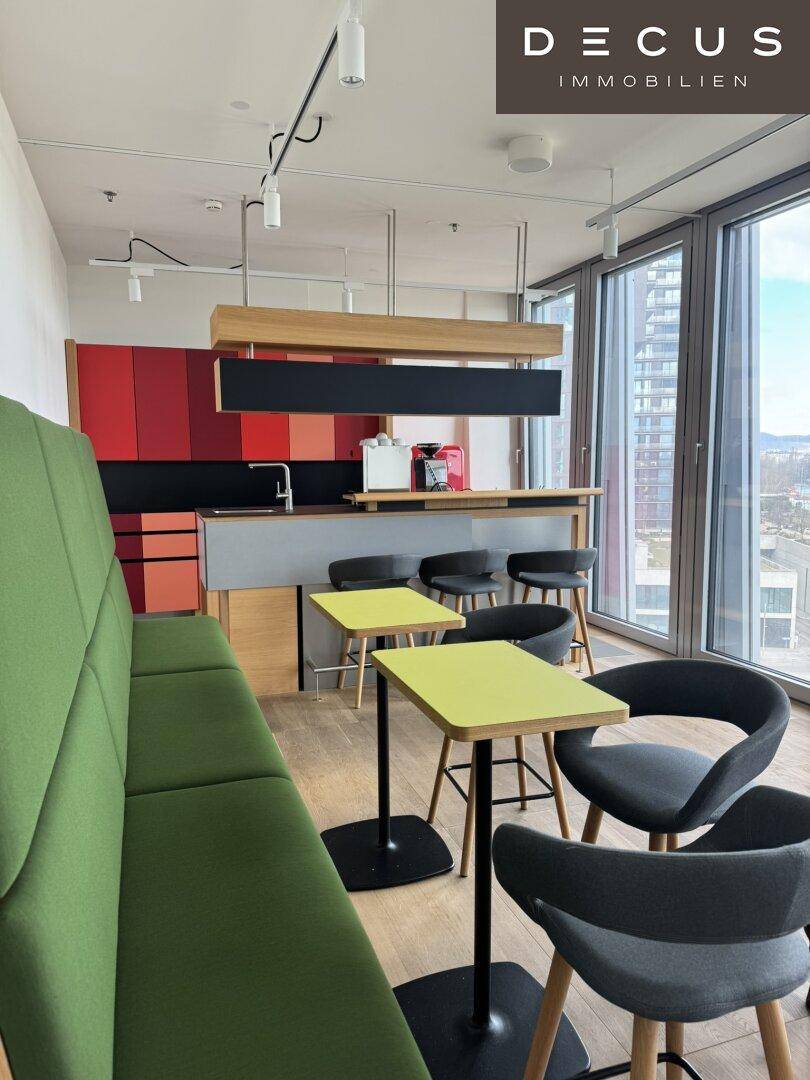 Lebhafter Lounge-Bereich mit grünen Sitzbänken, kleinen Tischen und einer modernen Küchenzeile.