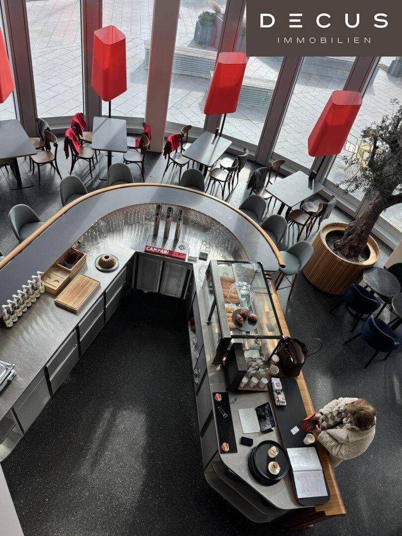Modernes Café mit Bar, Sitzgelegenheiten und Panoramablick auf die Stadt.