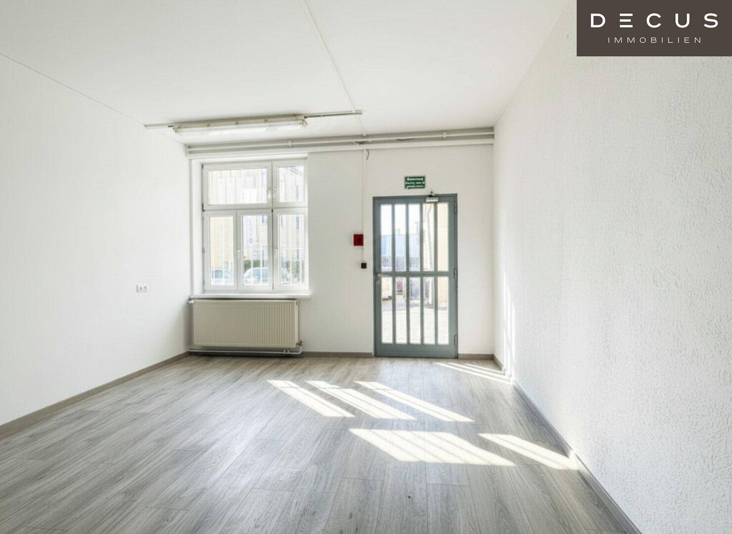 Heller, leerer Raum mit Laminatboden, weißen Wänden und einer Glastür, durch die Sonnenlicht fällt.