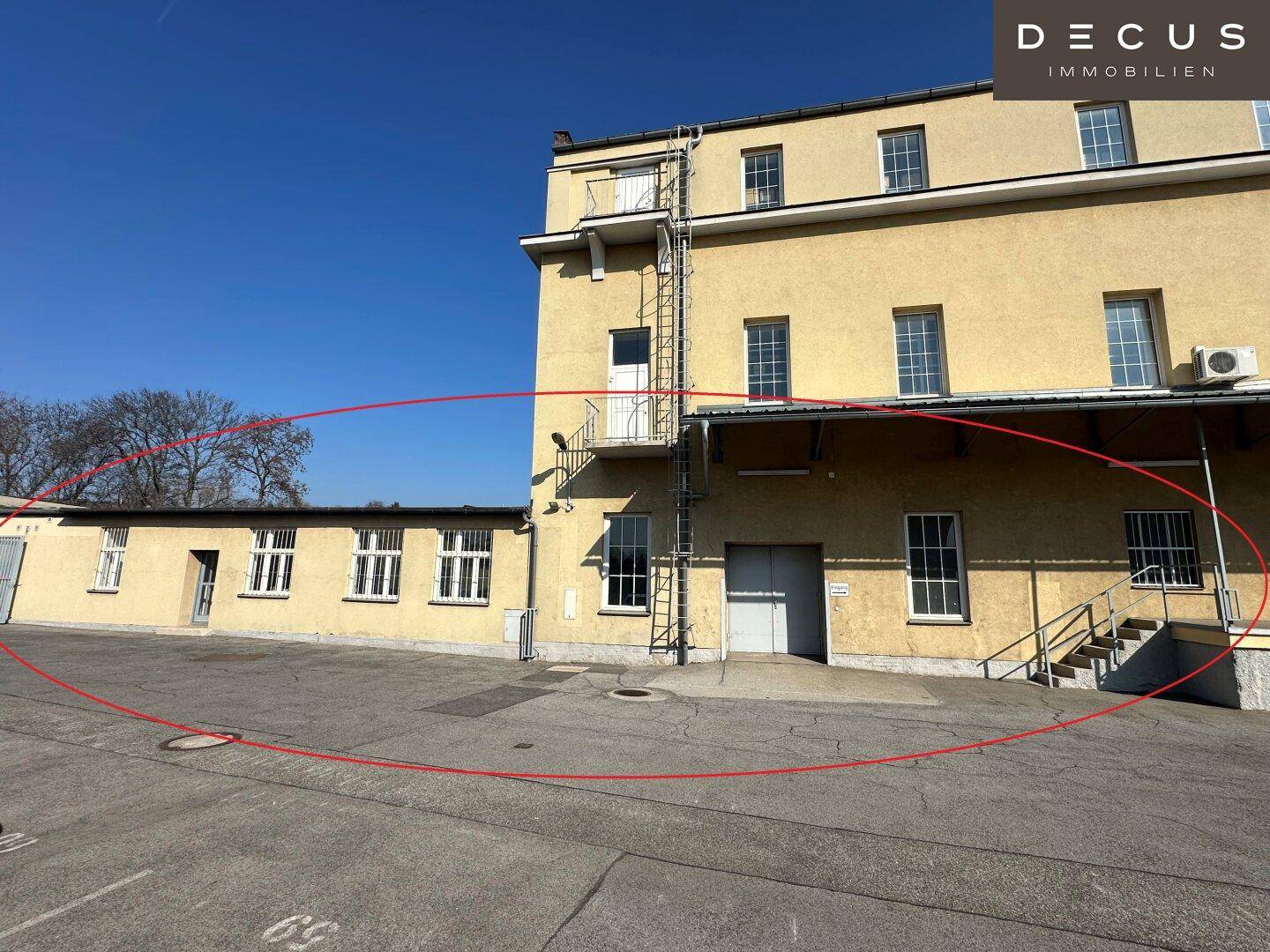 Großes Gewerbegebäude mit vielen Fenstern, Außentreppe und Laderampe, umgeben von einer Freifläche.