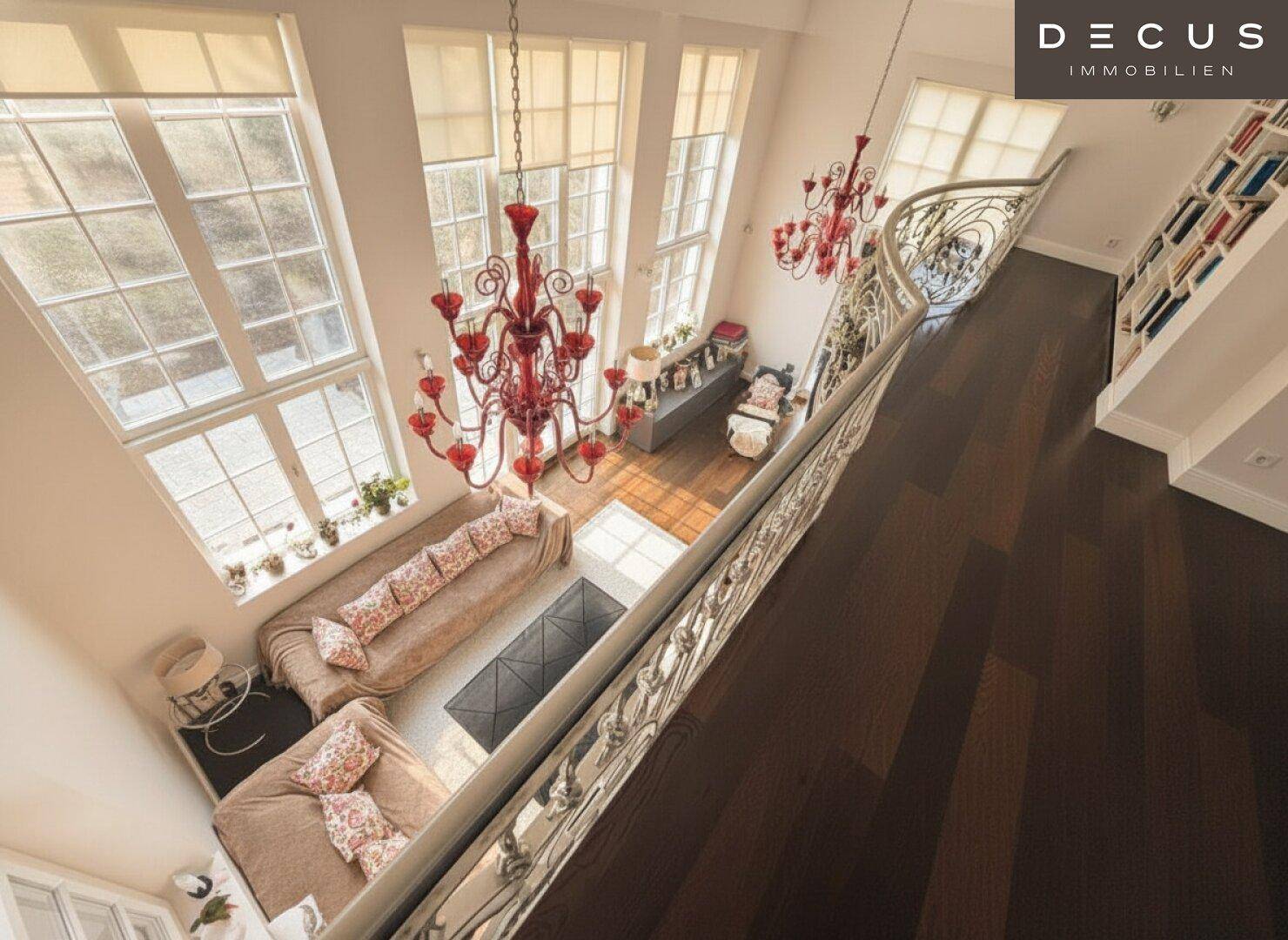 Blick von oben auf das lichtdurchflutete Wohnzimmer mit hohen Fenstern und eleganten Kronleuchtern.