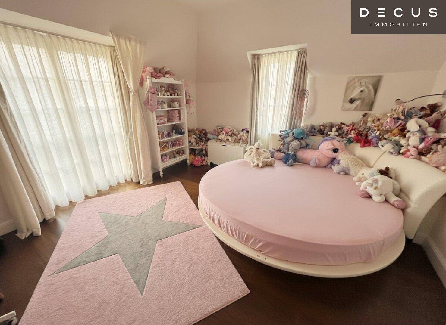Kinderzimmer mit rundem Bett, vielen Stofftieren und großen Fenstern für viel Tageslicht.