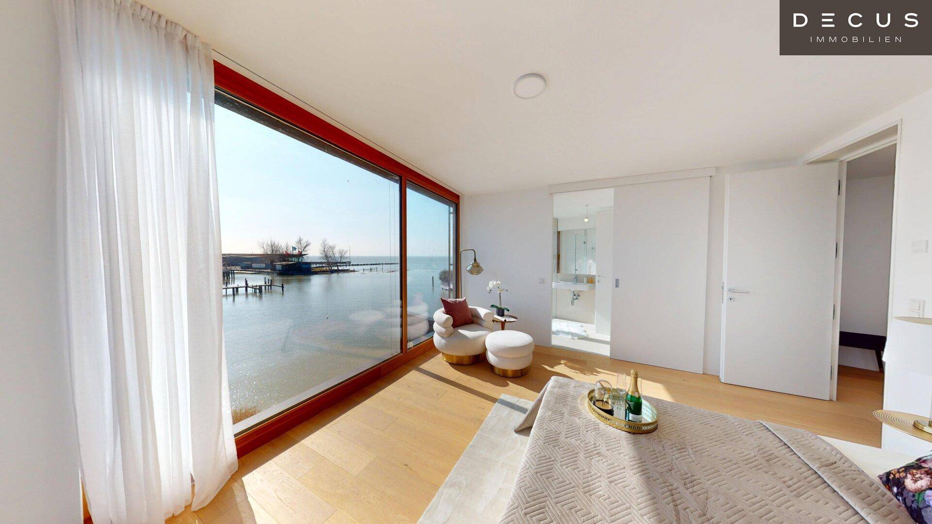 Schlafzimmer mit Panoramablick auf den See, großen Fenstern und hellem Parkettboden.