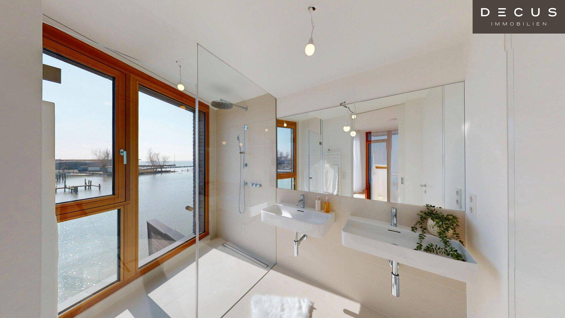 Modernes Badezimmer mit Doppelwaschbecken, großer Dusche und Seeblick durch Panoramafenster.