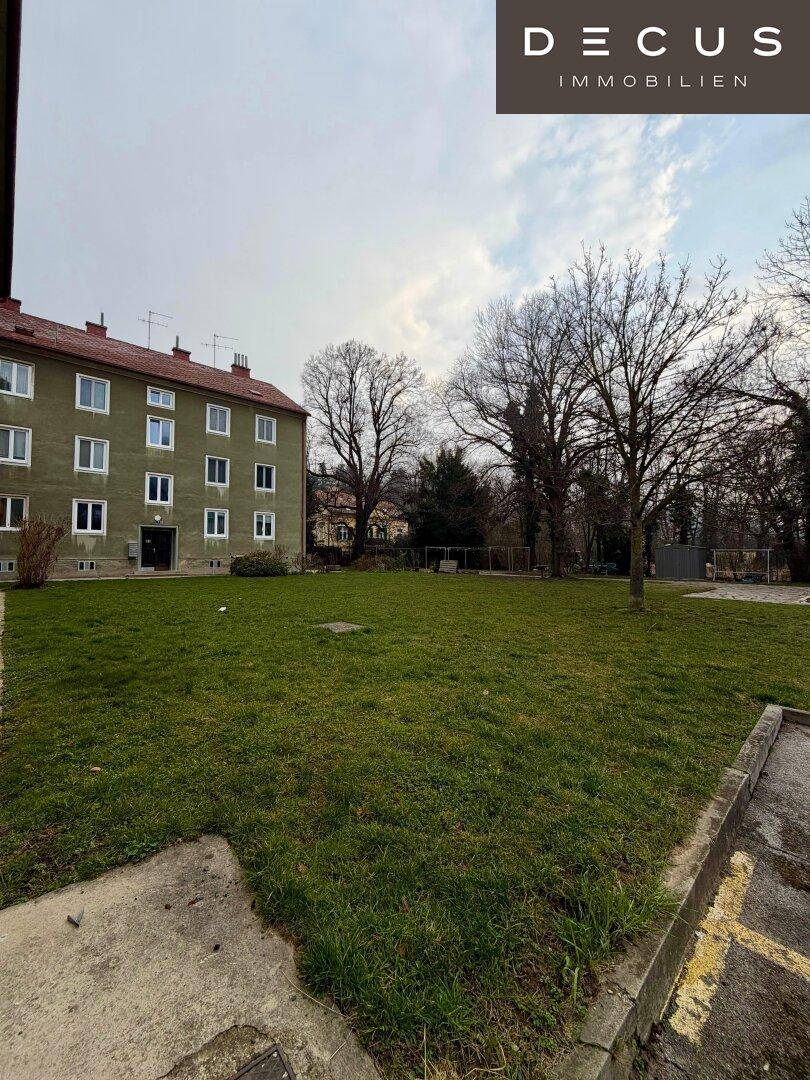 Eine offene Rasenfläche vor einem Wohngebäude mit vielen Fenstern.