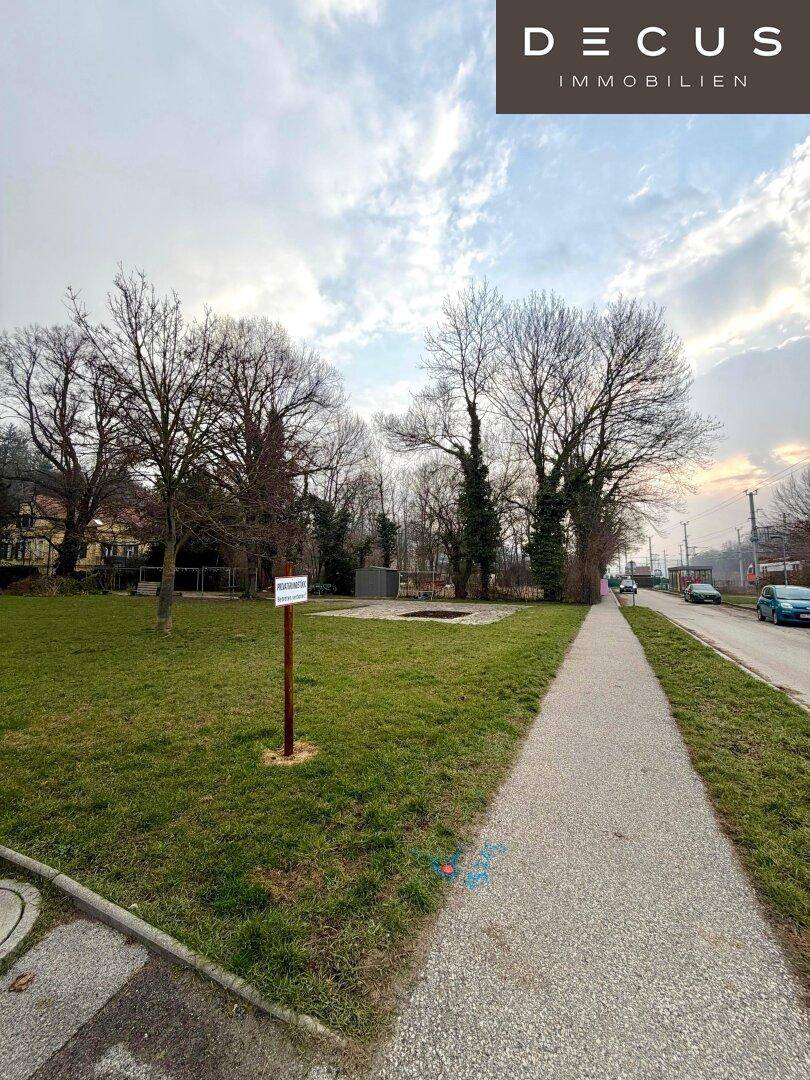 Ein Gehweg entlang einer Grünfläche mit einem Schild und Gebäuden in der Ferne.