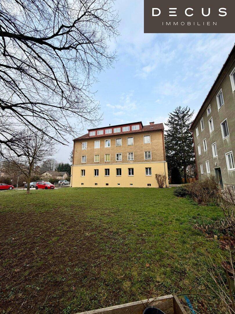 Ein Wohngebäude mit gelber Fassade und vielen Fenstern, umgeben von einer Grünfläche.