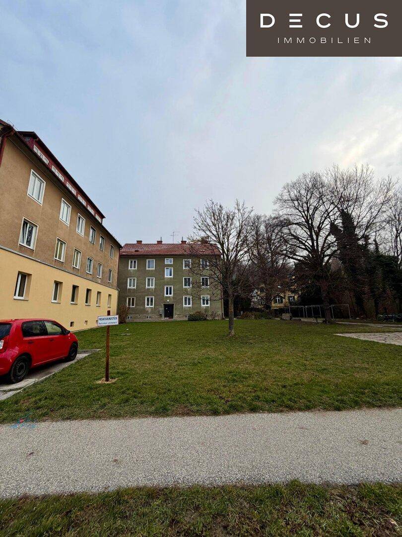 Eine Grünfläche vor Wohngebäuden mit einem geparkten roten Auto.