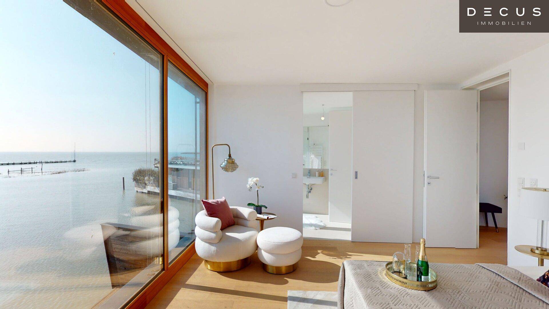 Helles Schlafzimmer mit Seeblick, großen Fenstern und direktem Zugang zum Badezimmer.