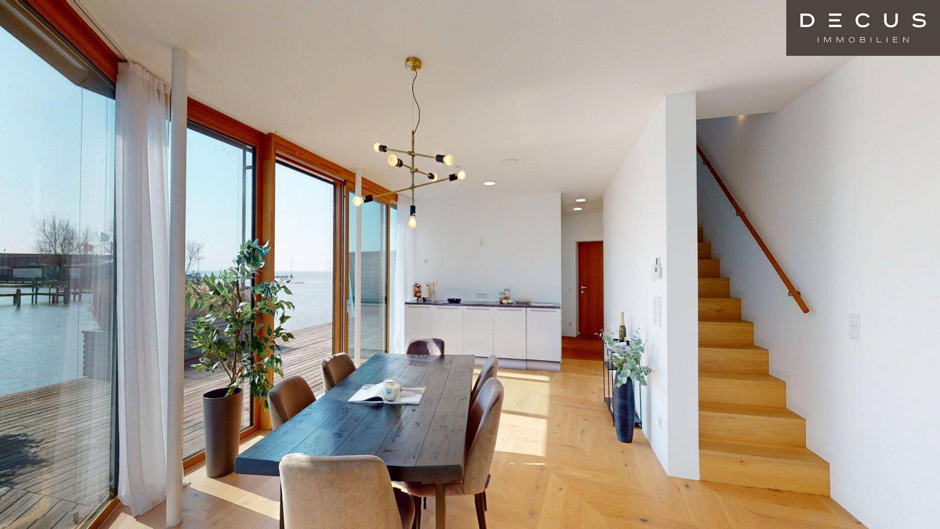 Offener Wohnbereich mit Essplatz, moderner Küche und Zugang zur Terrasse mit Seeblick.