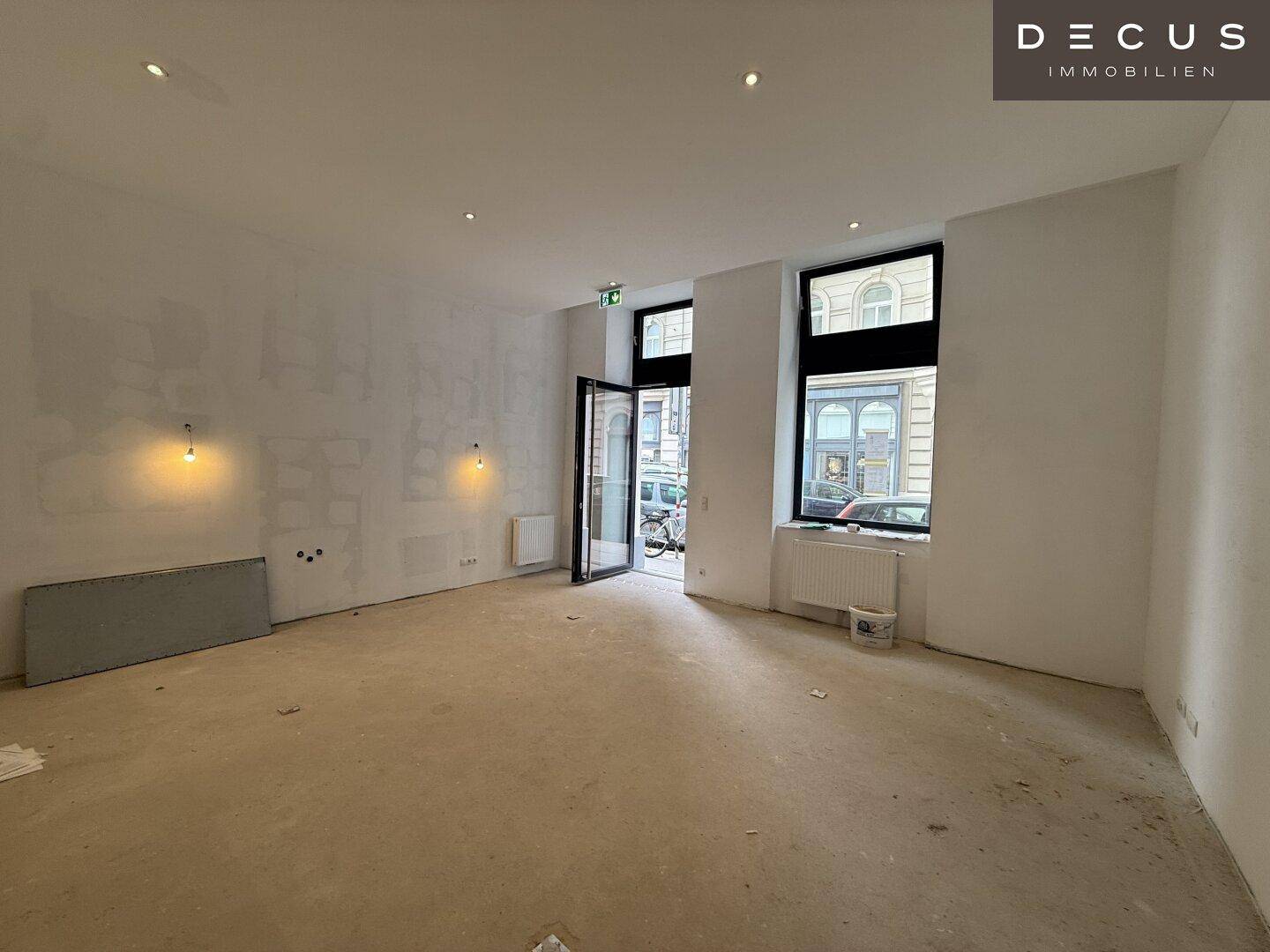 Großer Gewerberaum mit hohen Fenstern zur Straße und viel Tageslicht, bereit für den Innenausbau.