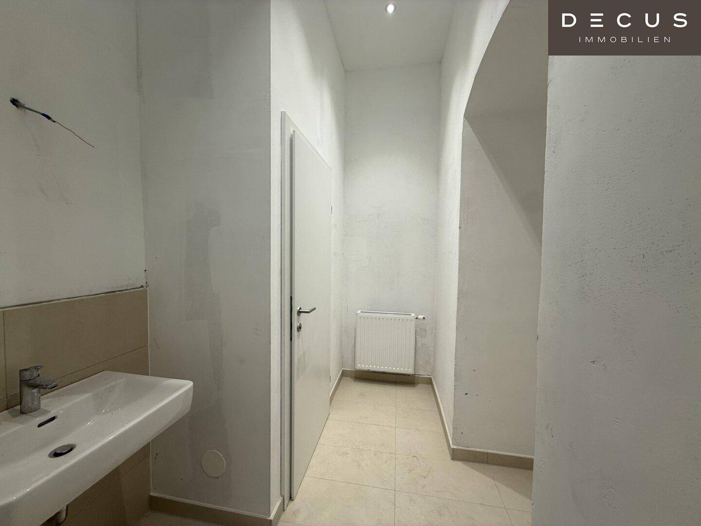 Eingangsbereich zu einer modernen Gästetoilette mit Waschbecken und hellen Fliesen, in gutem Zustand.