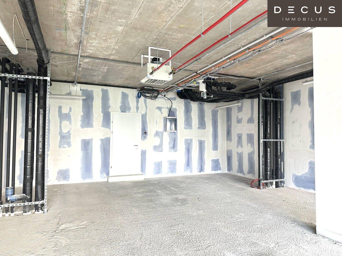Rohbau eines Gewerberaums mit freiliegenden Rohren und unfertigen Wänden, bereit für den Ausbau.
