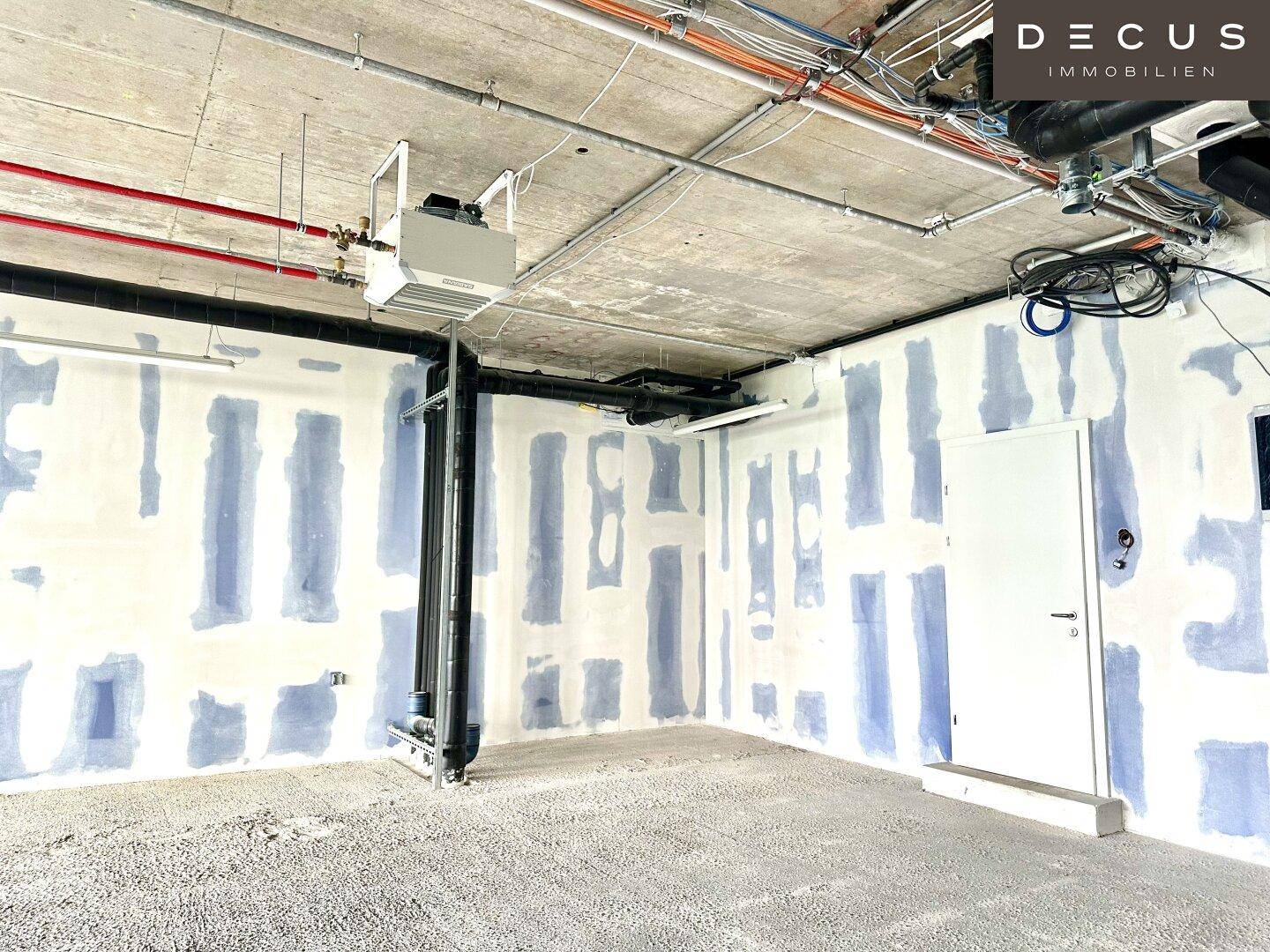 Innenansicht eines Gewerberaums im Rohbau mit sichtbaren Installationen und vorbereiteten Wänden.