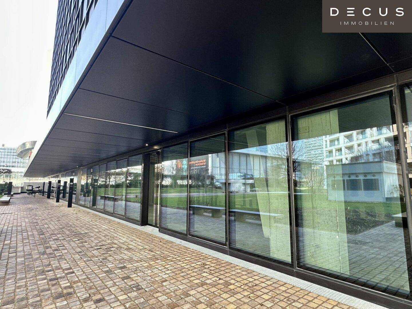 Weitläufige Glasfronten im Erdgeschoss eines modernen Bürogebäudes mit reflektierenden Oberflächen und Außenbereich.