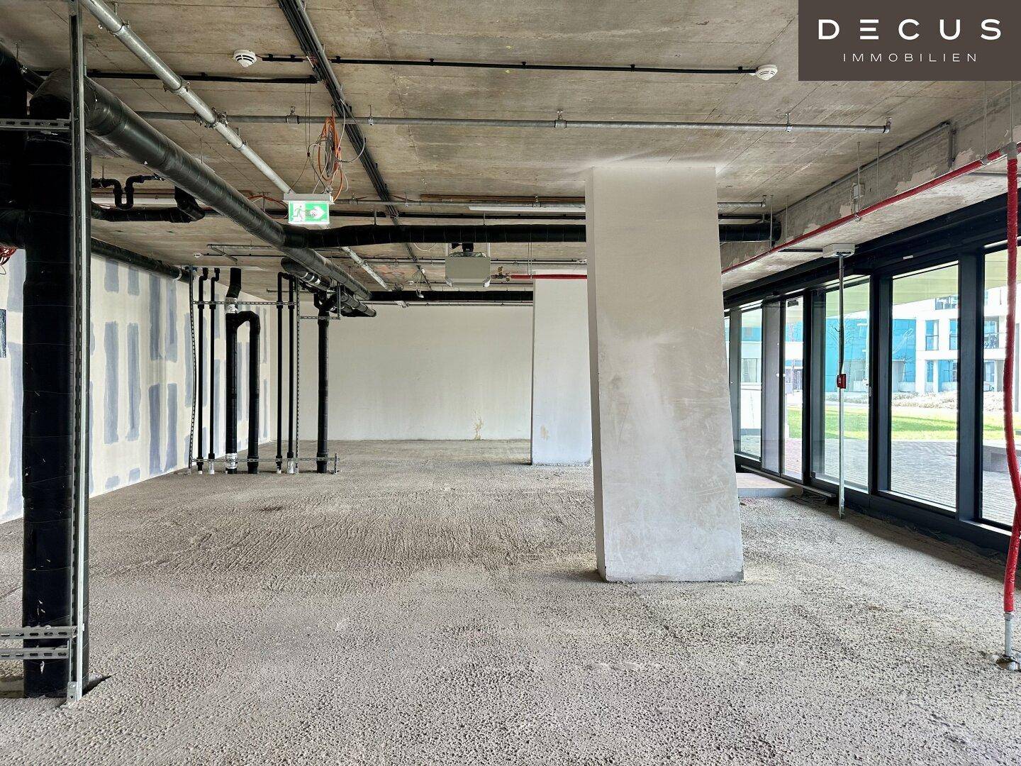 Großer, offener Raum im Rohbau mit sichtbaren Leitungen an der Decke und hohen Decken im Bürogebäude.