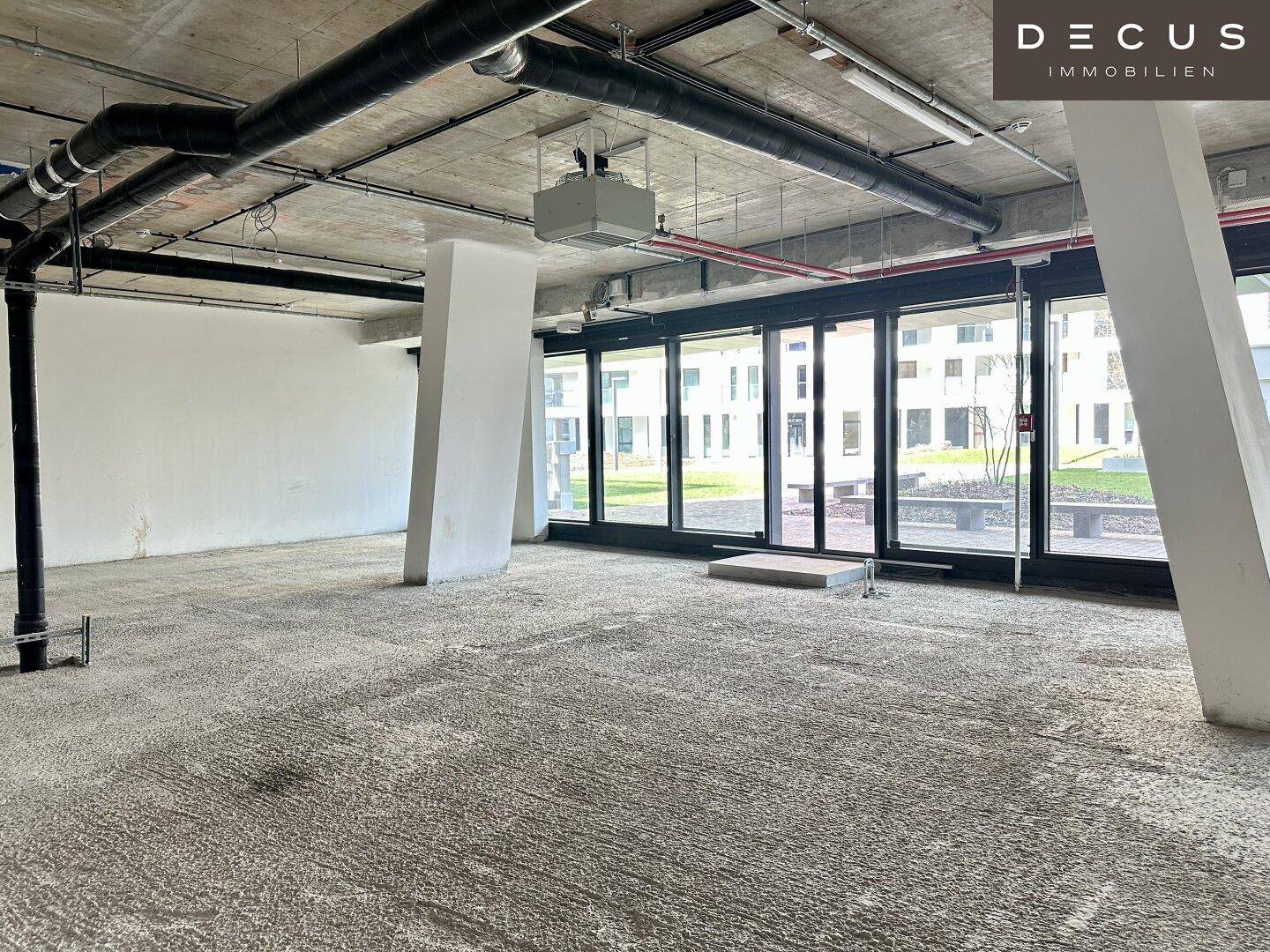Heller Rohbau mit großen Fensterfronten, die viel Tageslicht hereinlassen und einen grünen Ausblick bieten.