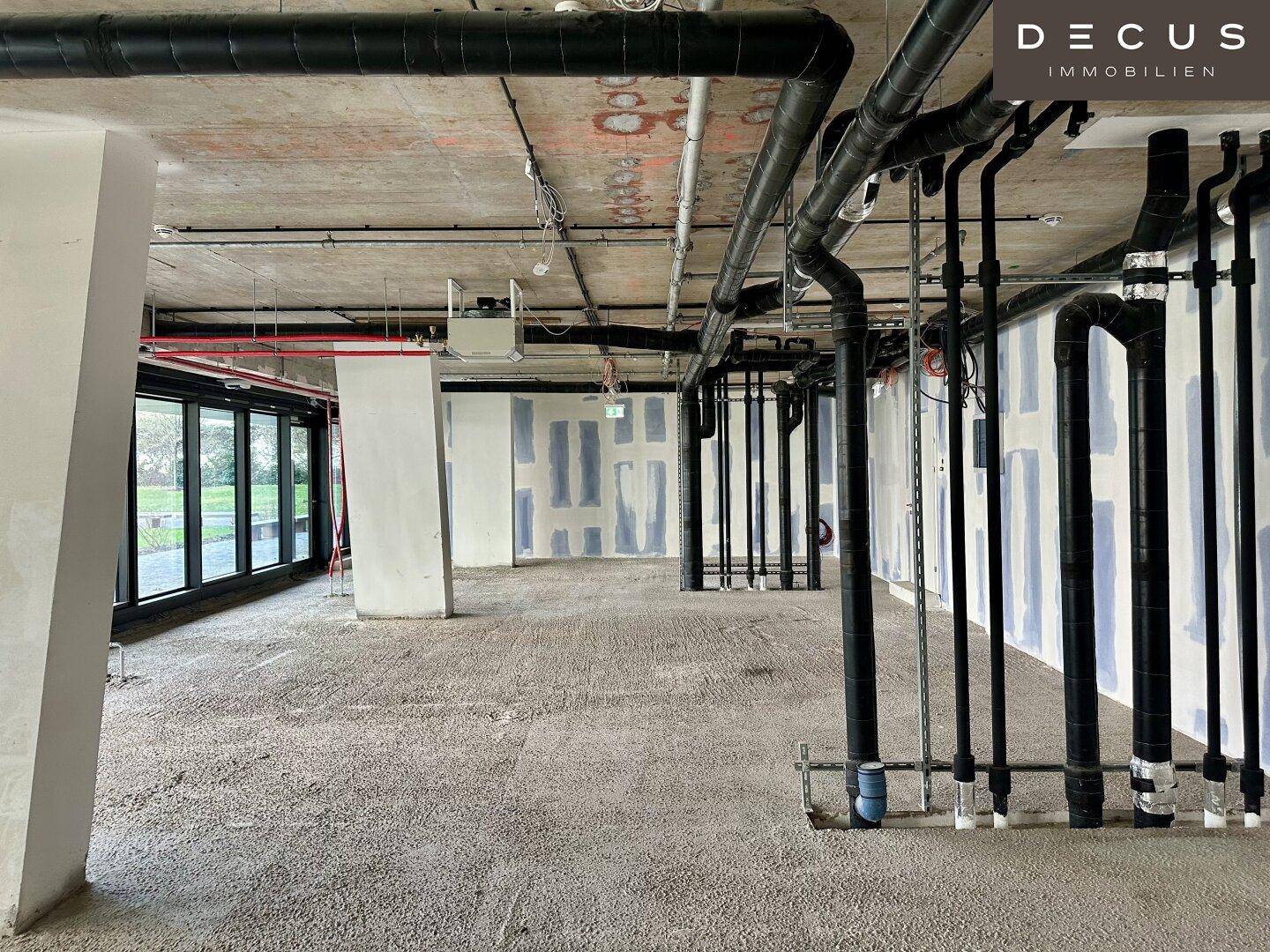 Unfertiger Innenraum mit zahlreichen sichtbaren Rohren und Leitungen an Decke und Wänden im Rohbauzustand.