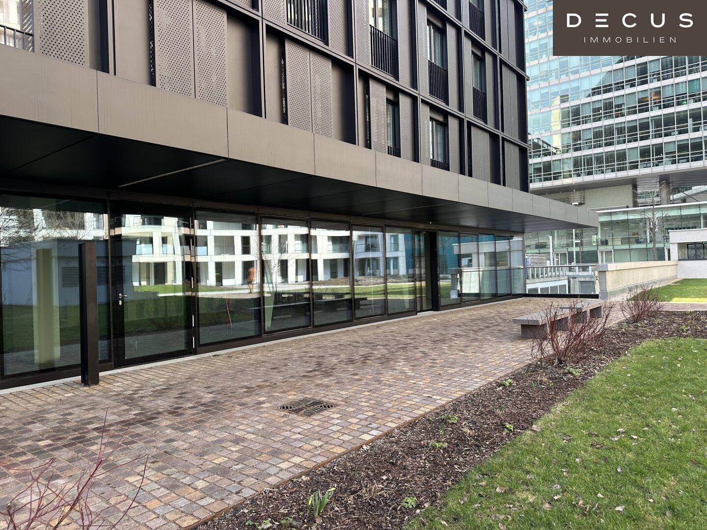 Erdgeschossfassade eines modernen Gebäudes mit großen Glasfronten und gepflastertem Gehweg im Freien.