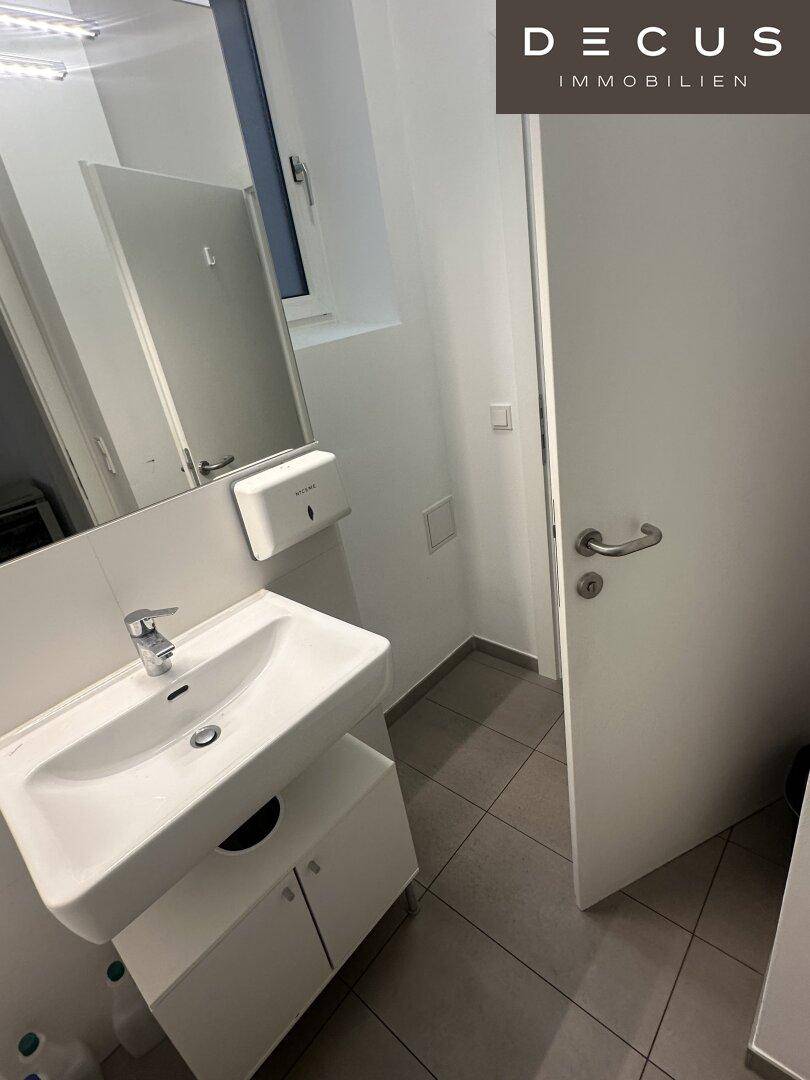 Modernes Badezimmer mit Waschbecken, Spiegel und einem Fenster für Tageslicht.