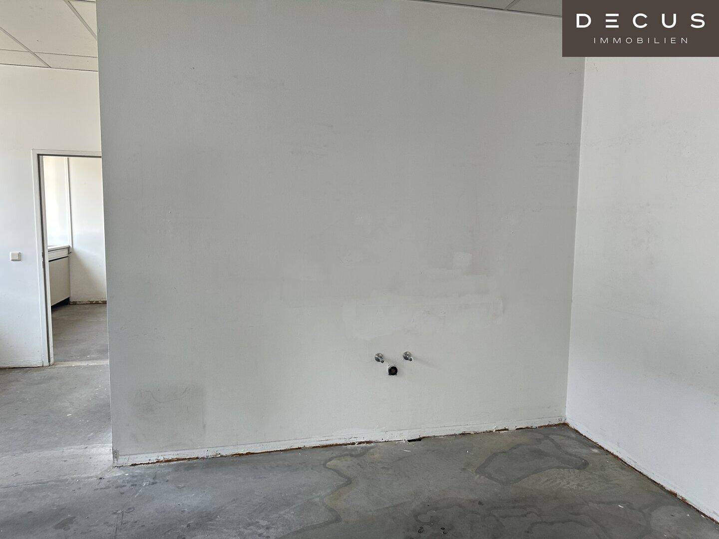Weiße Wand mit Anschlüssen und Blick auf einen kleinen Küchenbereich im Hintergrund.