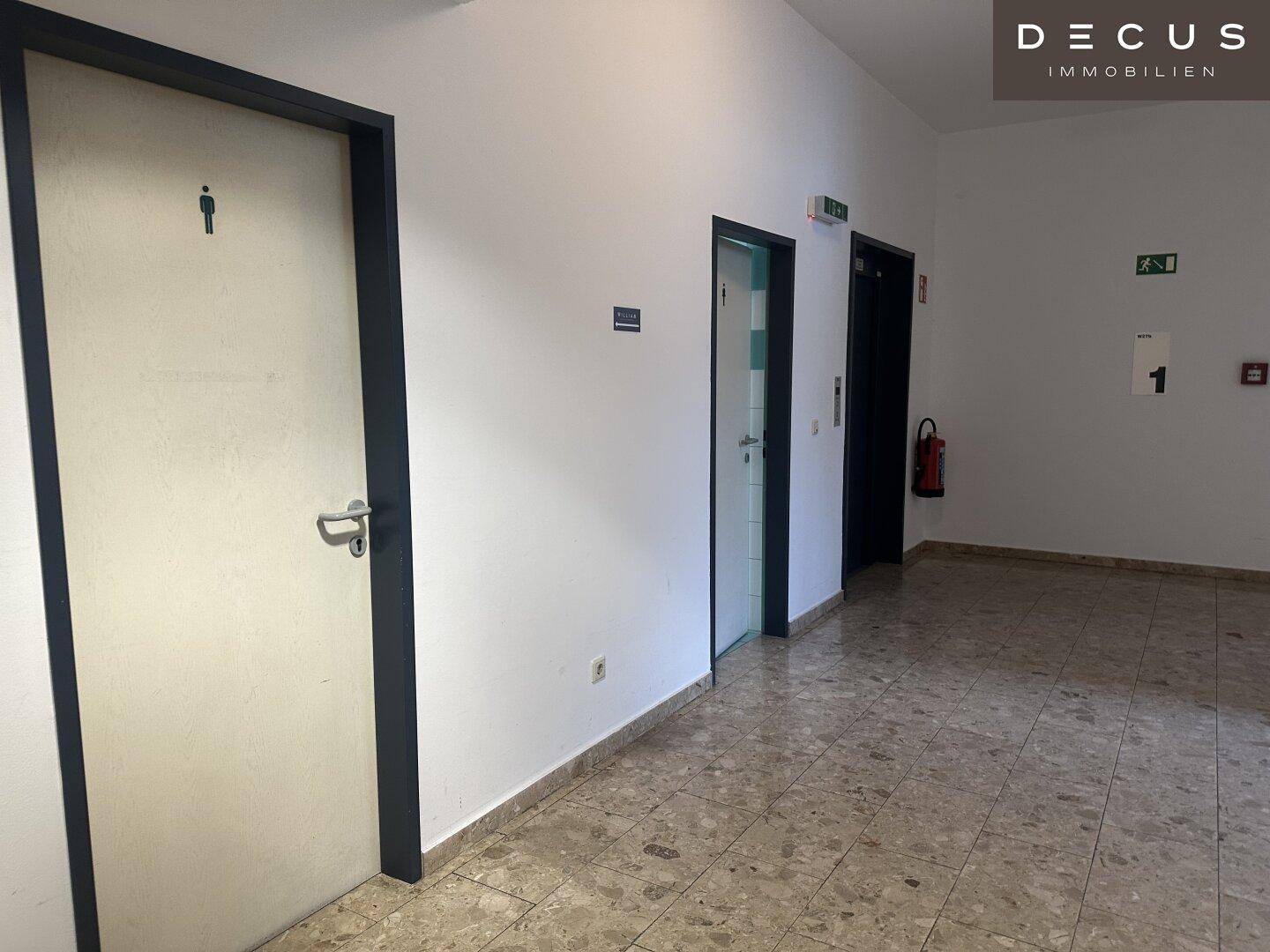 Eingangsbereich oder Flur mit mehreren Türen, darunter eine Toilette, und einem gemusterten Fliesenboden.