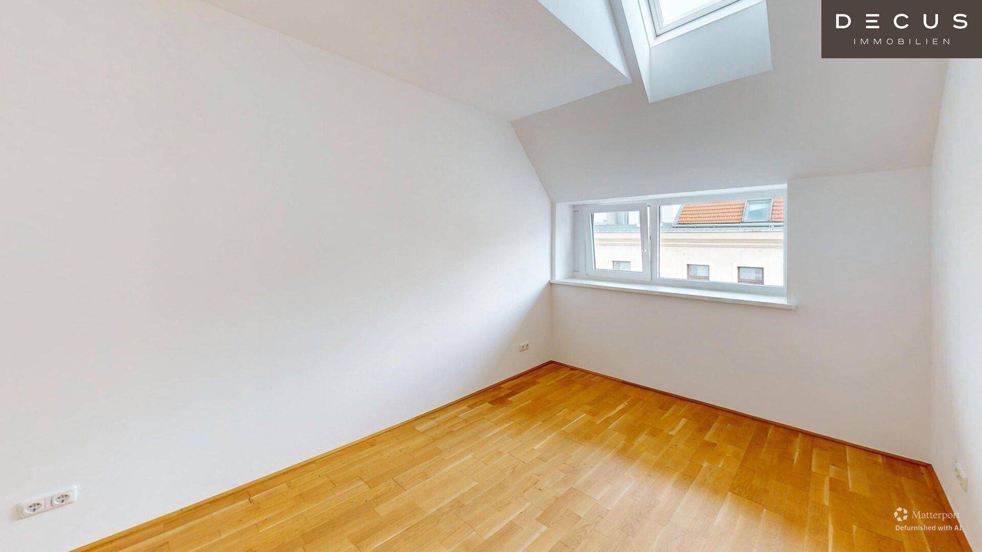 Geräumiges Zimmer im Dachgeschoss mit Holzboden und einem Fenster mit Blick auf die Umgebung.