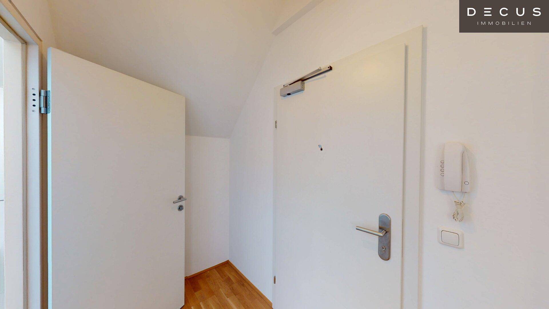 Eingangsbereich mit Holzboden, weißer Tür und Gegensprechanlage.
