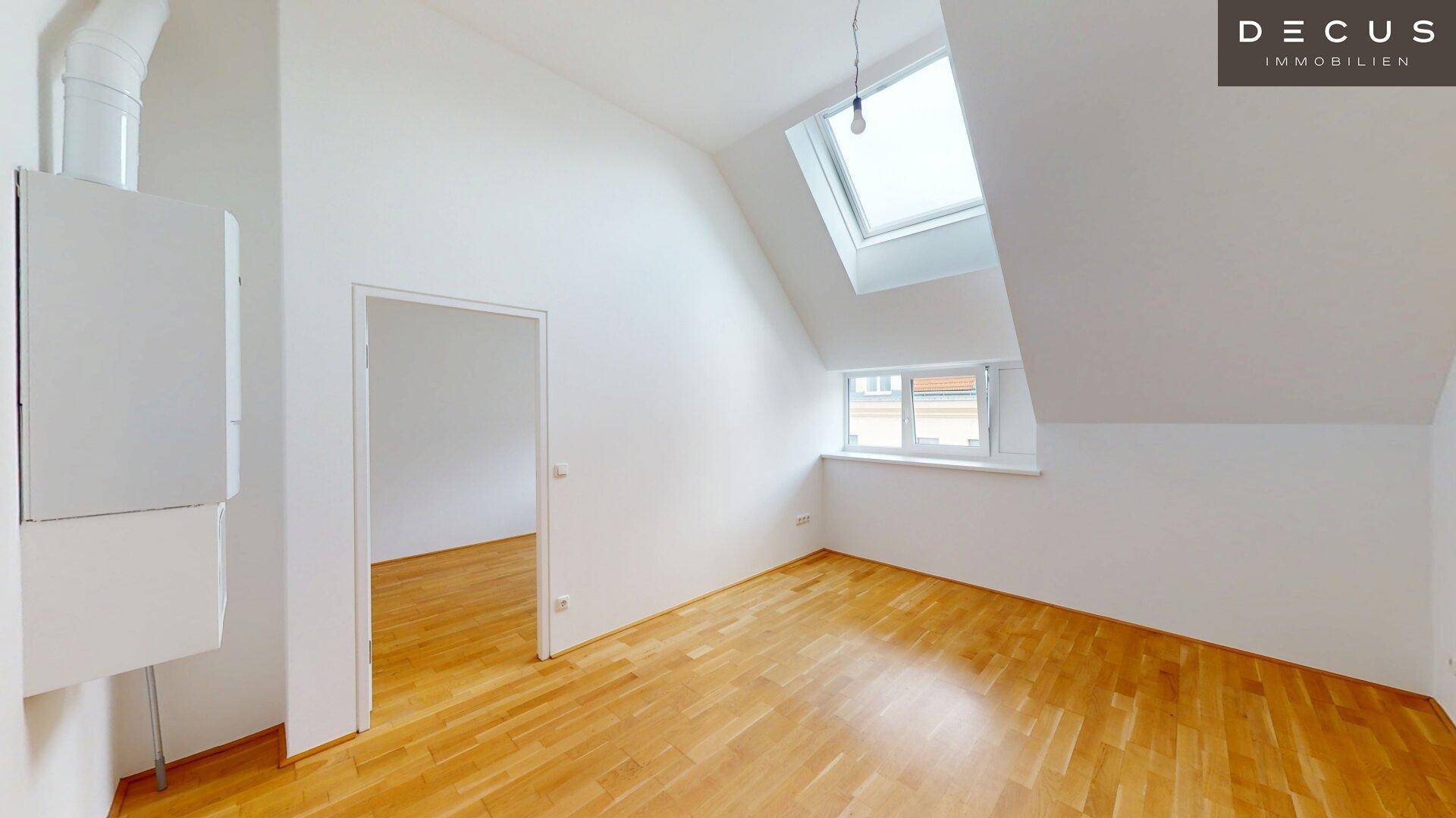 Helles Zimmer mit Holzboden, Dachschrägen und einem Heizkessel an der Wand.