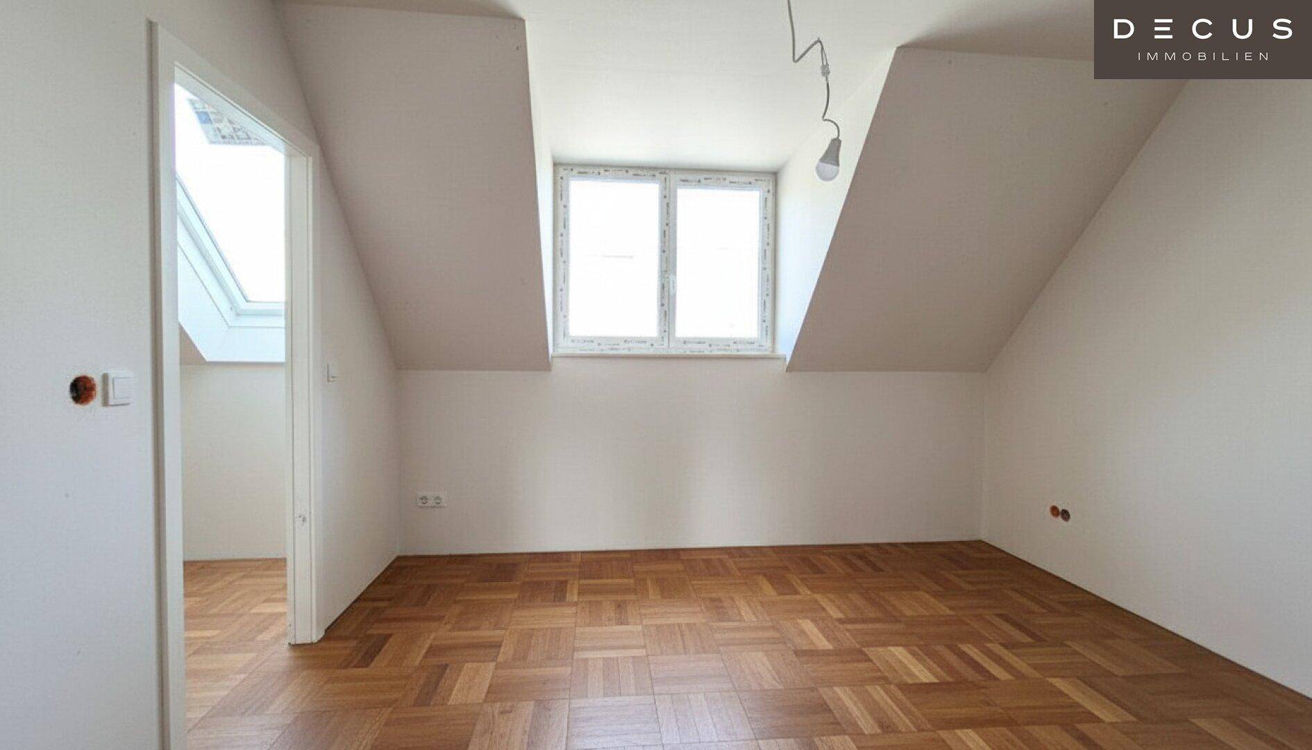 Leeres Dachgeschosszimmer mit schrägen Wänden und Fischgrätparkett, das auf seine Nutzung wartet.