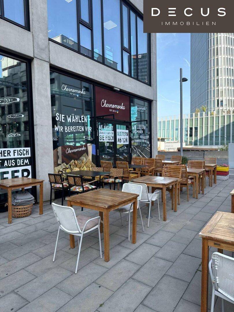 Großer Außenbereich mit vielen Holztischen und Stühlen vor dem Restaurantgebäude.