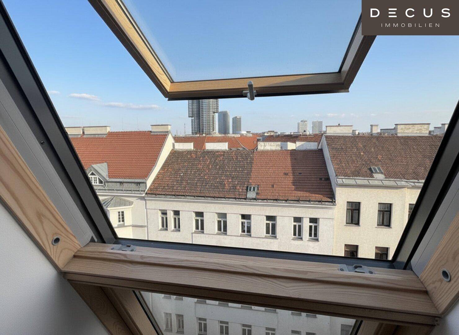 Weitblick über die Dächer der Stadt durch ein geöffnetes Dachfenster, mit moderner Skyline im Hintergrund.