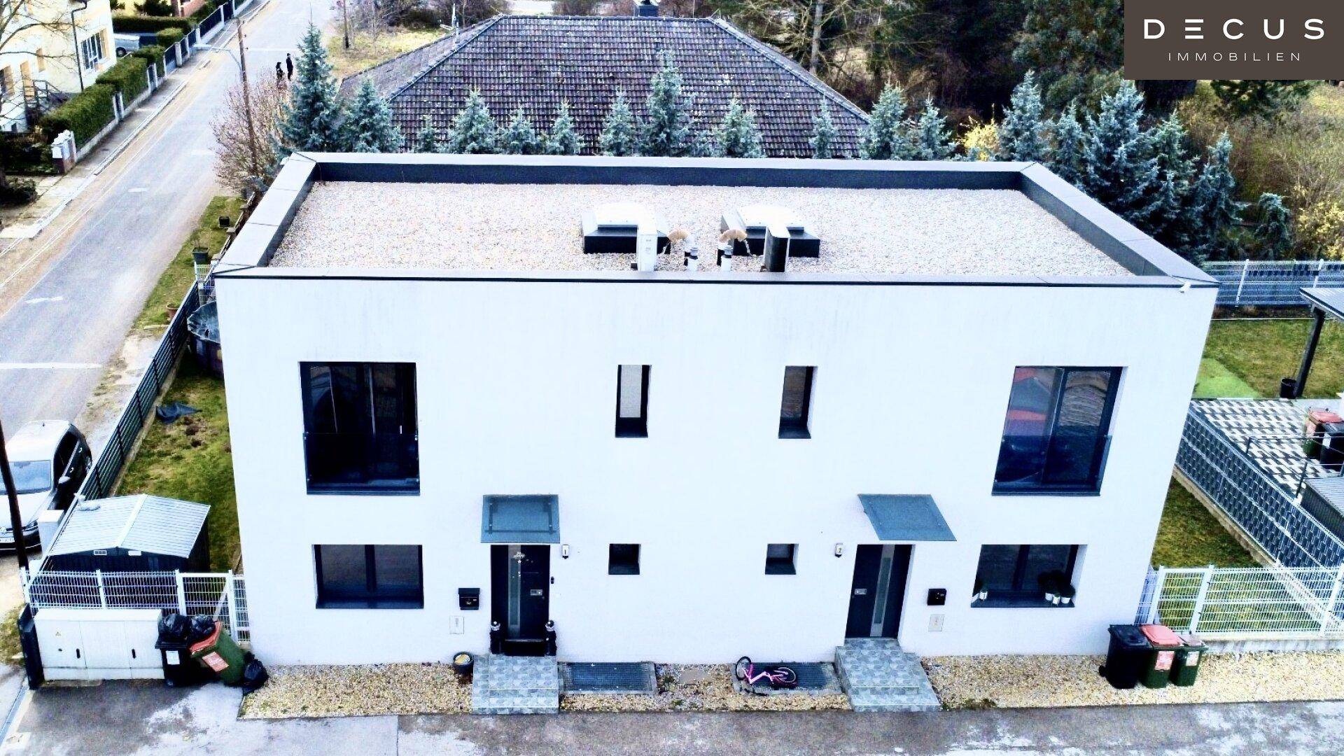 Moderne Doppelhaushälfte mit Flachdach und großen Fenstern in ruhiger Wohngegend.