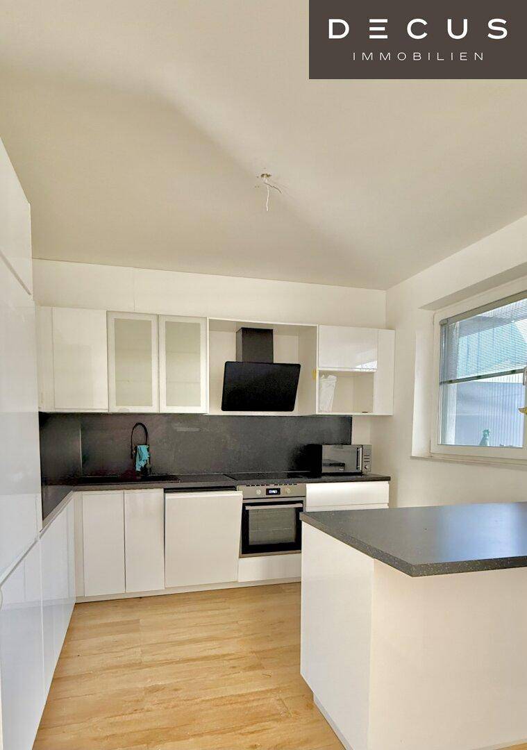 Moderne Einbauküche mit weißen Hochglanzschränken, dunkler Arbeitsplatte und Fenster.