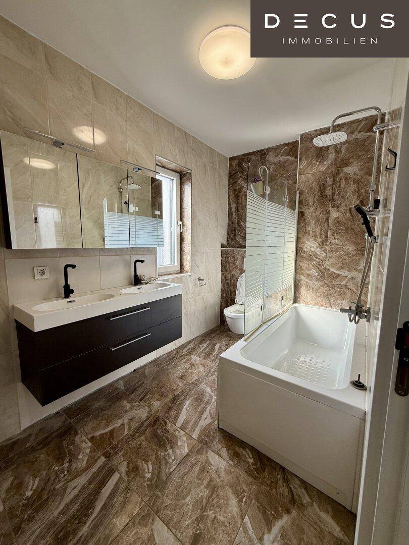 Modernes Badezimmer mit Doppelwaschbecken, Badewanne und Dusche in Brauntönen.