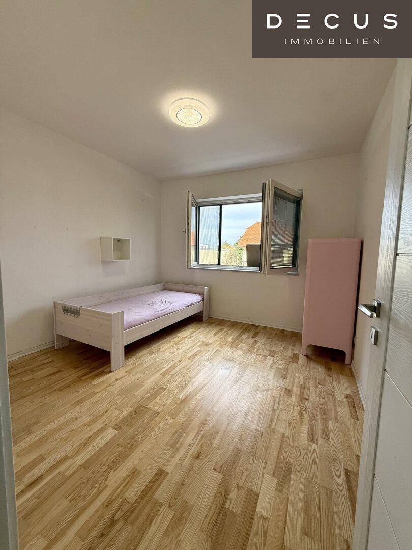 Helles Schlafzimmer mit Parkettboden und großem Fenster, ideal für Kinder oder Gäste.