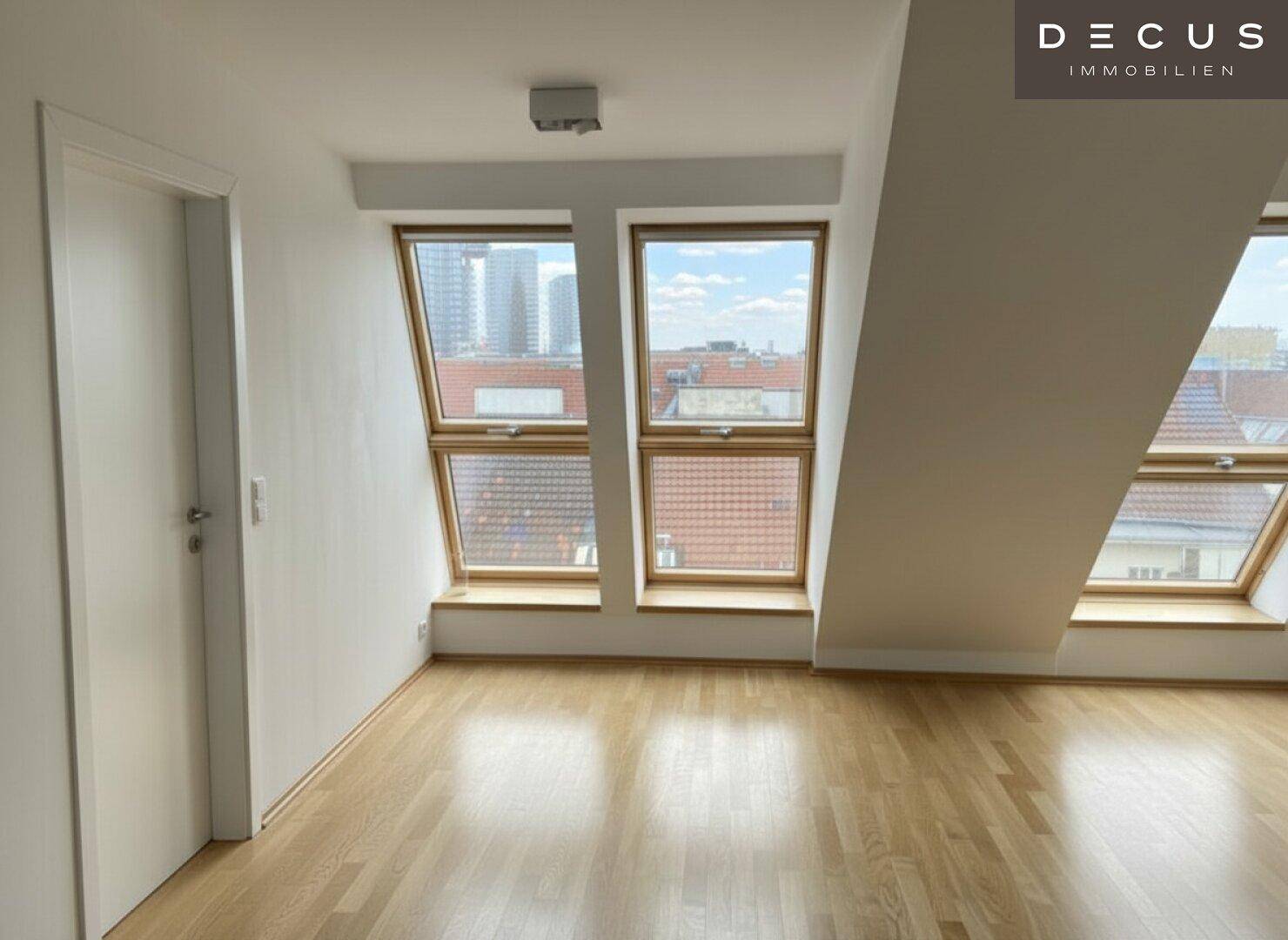 Heller Dachbodenraum mit Holzboden und großen Fenstern, die einen weiten Blick über die Stadt bieten.