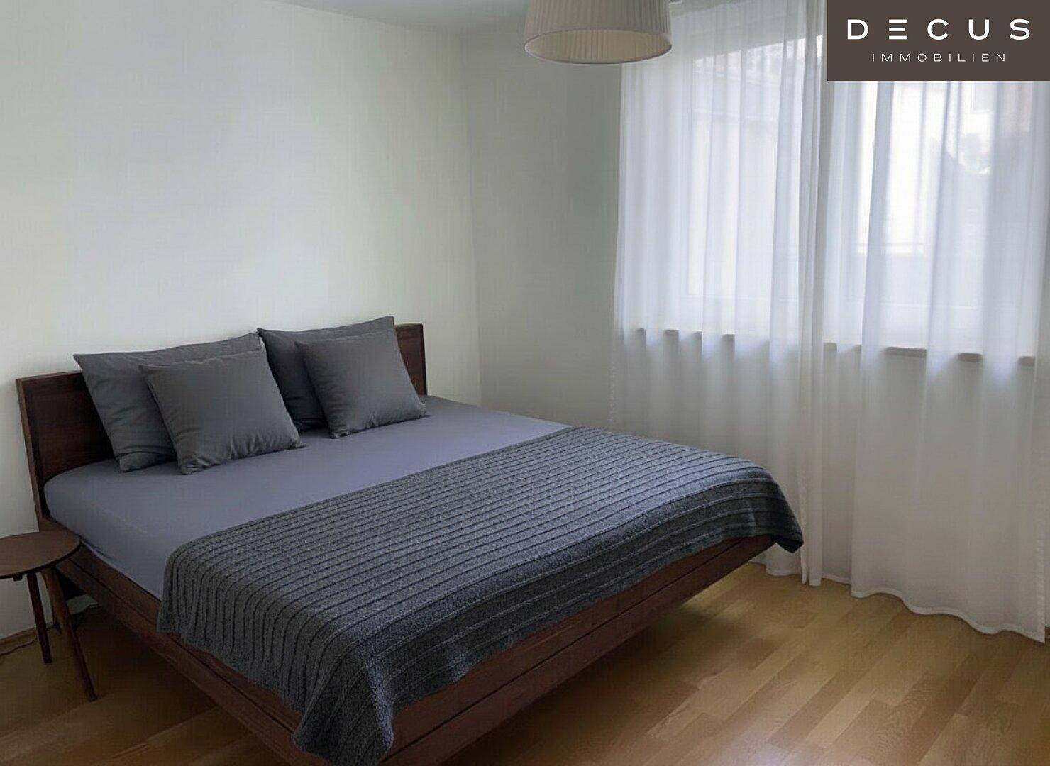 Gemütliches Schlafzimmer mit Holzboden, Doppelbett und großen Fenstern, die viel Tageslicht hereinlassen.