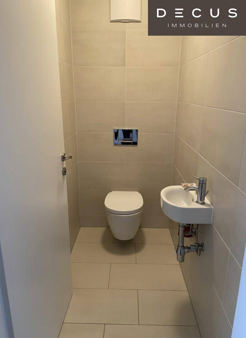 Modernes Gäste-WC mit hellen Fliesen, wandhängendem WC und kleinem Waschbecken.